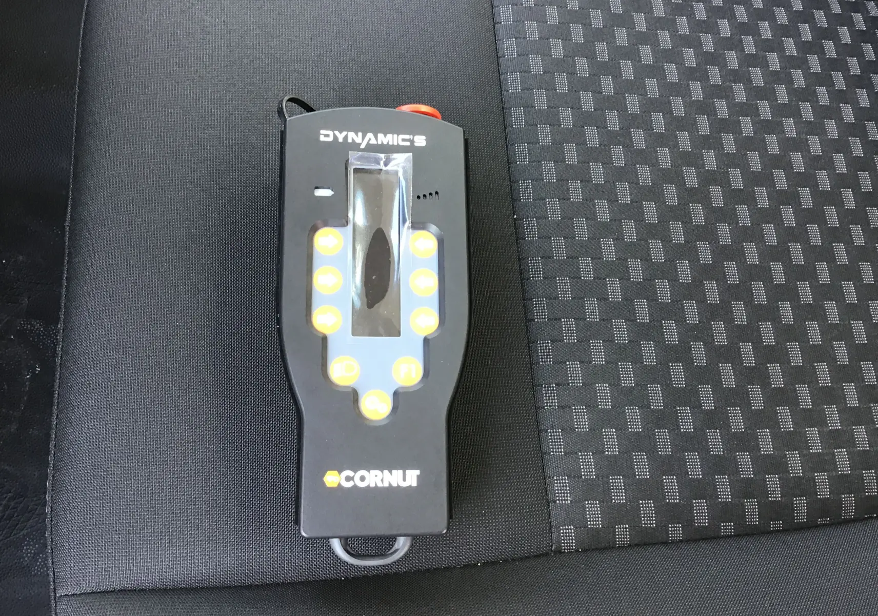 Télécommande noire du bras Polybenne Cornut posée sur un siège tissu gris foncé à motifs du Ford Transit Chassis Cabine blanc.