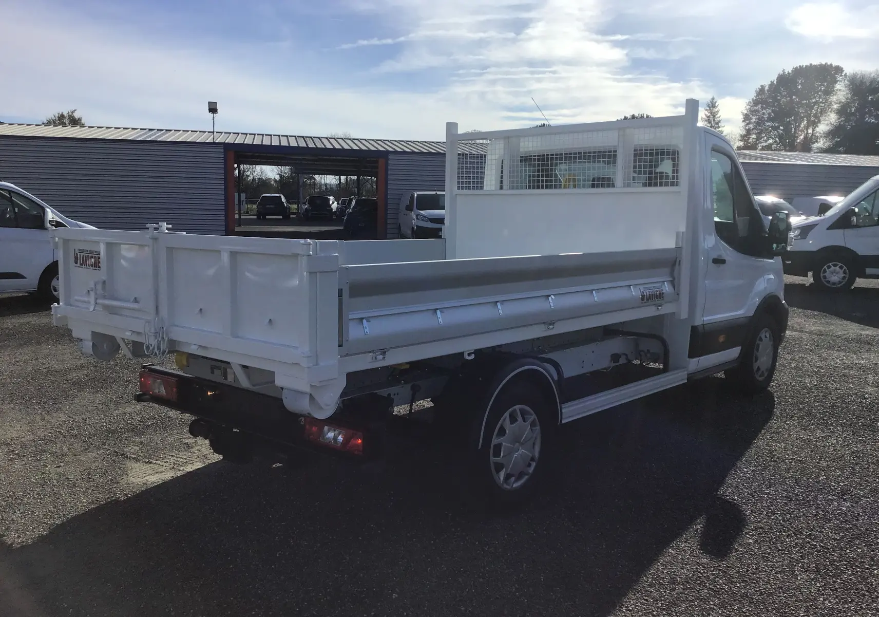 Ford Transit Chassis Cabine blanc vu en 3/4 arrière droit avec benne basculante et bras polybenne sur parking.