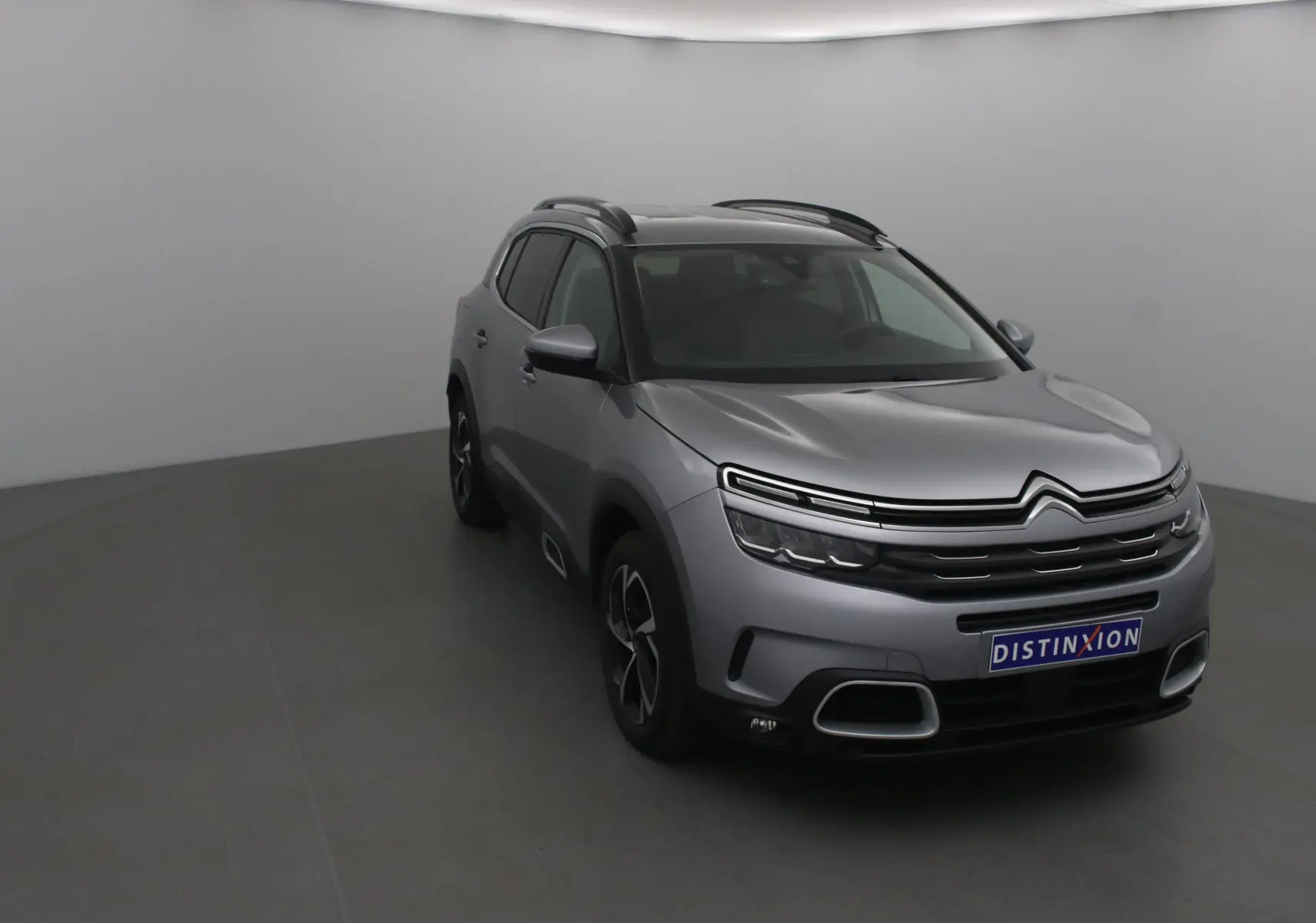 Citroën C5 Aircross gris Artense vu en 3/4 avant droit dans un studio avec calandre distinctive et jantes noires.