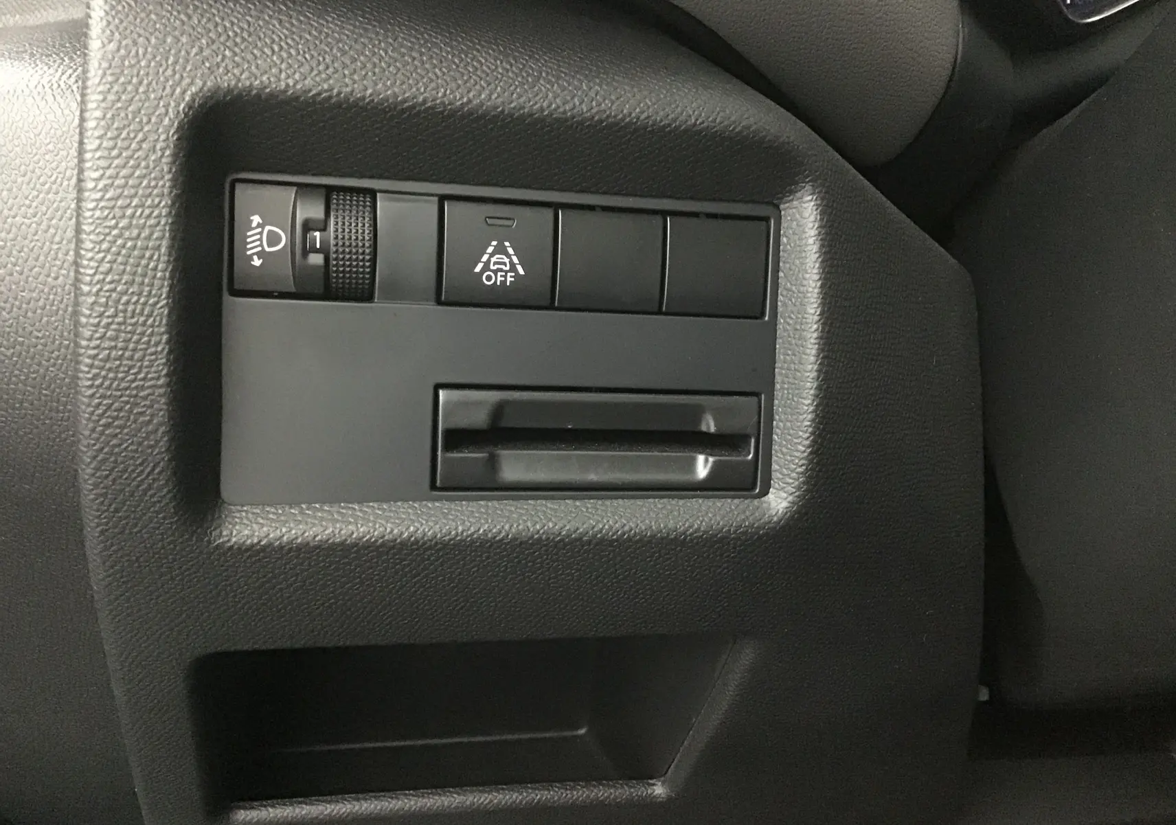 Gros plan sur les commandes de réglage des phares et d'aide à la conduite du tableau de bord noir d'une Citroën C5 Aircross gris Artense.