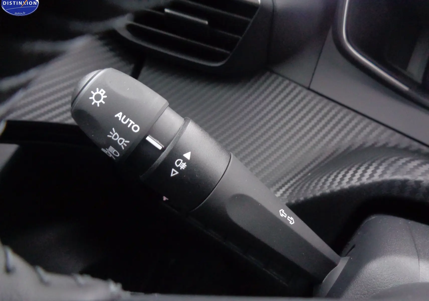 Gros plan sur la commande des feux automatique dans l'habitacle au design carbone du Peugeot 2008 bleu Vertigo 2023.