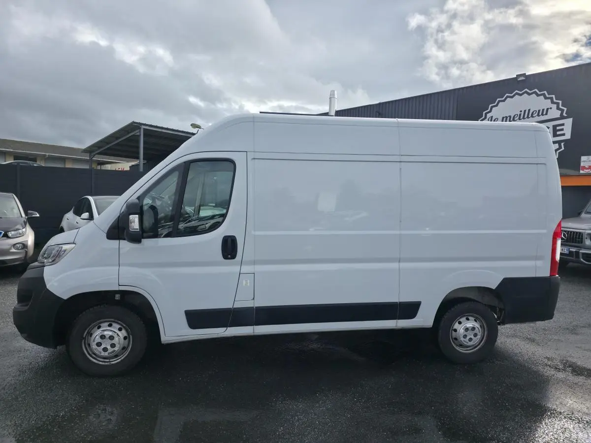 Profil côté gauche d'un fourgon Opel Movano blanc avec panneaux latéraux bois et porte coulissante tôlée.