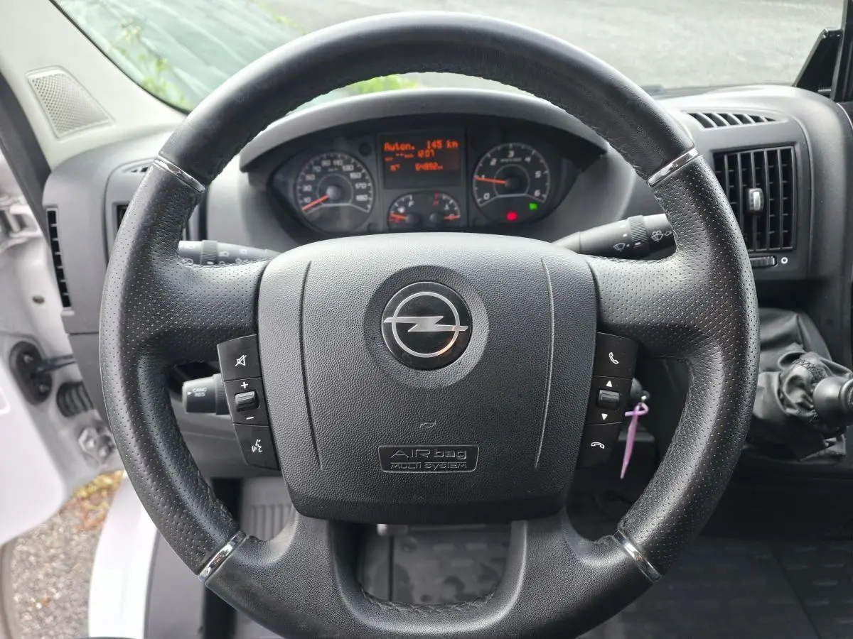 Volant noir perforé avec logo Opel au centre, tableau de bord numérique et levier de vitesses manuel visible côté droit.