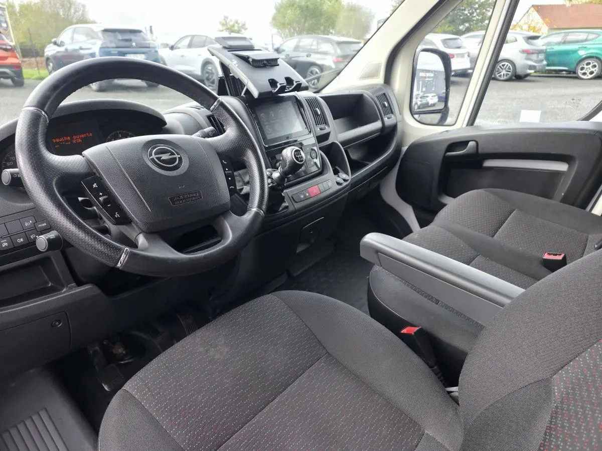 Intérieur de l’Opel Movano Fourgon 2022 vu côté conducteur, avec volant noir et sièges tissu gris foncé à motifs rouges.