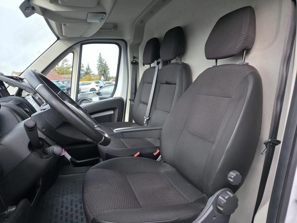 Vue intérieure côté conducteur de l'Opel Movano blanc, montrant les sièges en tissu gris foncé et le volant noir.