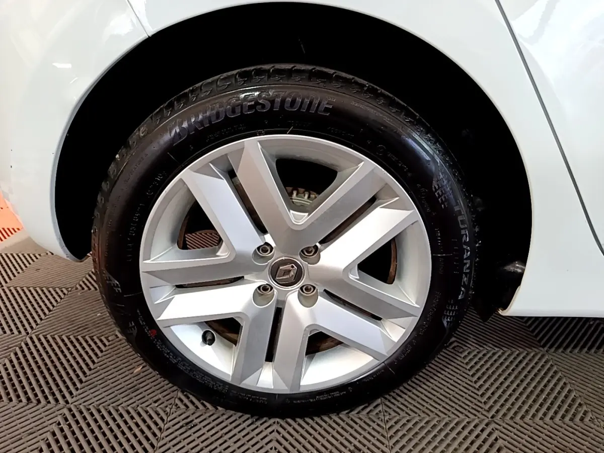 Gros plan sur la roue avant droite d'une Renault Clio blanche, jante alliage argentée avec logo Renault au centre.