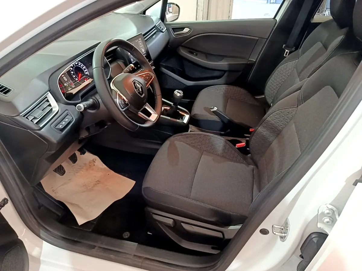 Vue intérieure côté conducteur de la Renault Clio Business blanche, avec volant cuir, tableau de bord numérique et sièges tissu gris.