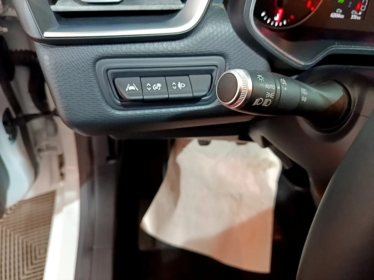 Vue intérieure rapprochée côté gauche du tableau de bord de la Renault Clio blanche, avec commandes d’aide à la conduite et commodo des phares.