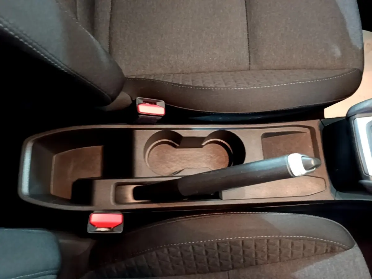 Vue plongeante sur la console centrale noire de la Renault Clio Business avec frein à main manuel et sièges tissu gris foncé.