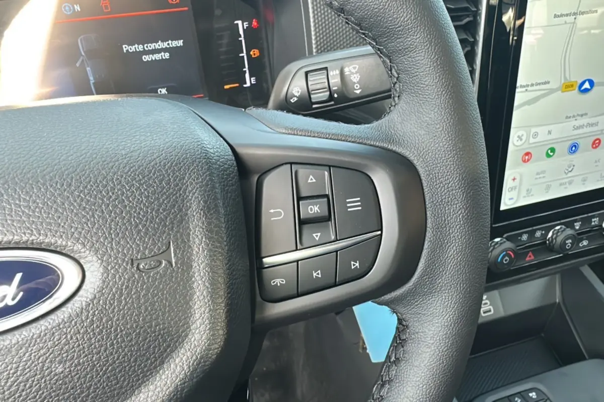 Gros plan sur le volant cuir noir du Ford Ranger 2026 avec commandes multifonctions et écran tactile visible à droite.