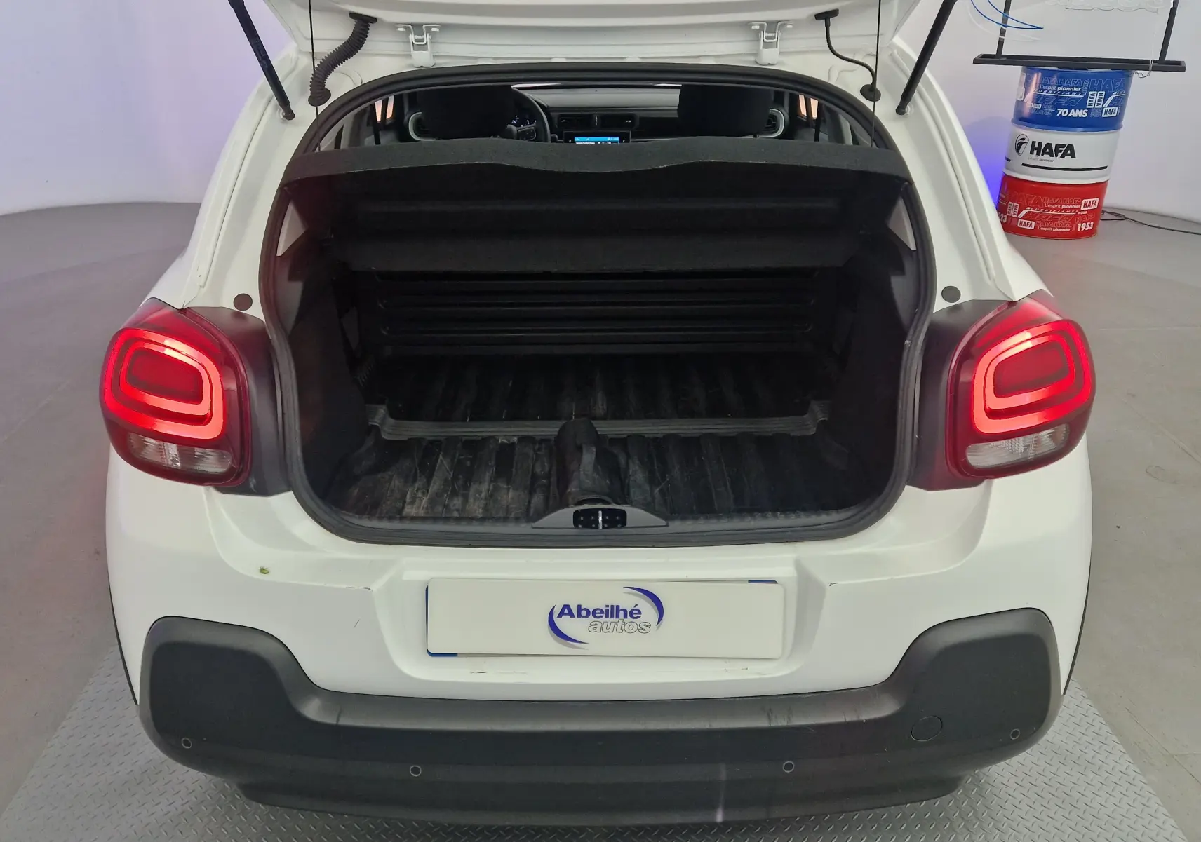 Vue arrière d'une Citroën C3 Société blanche de 2019 avec coffre ouvert et feux arrière allumés.