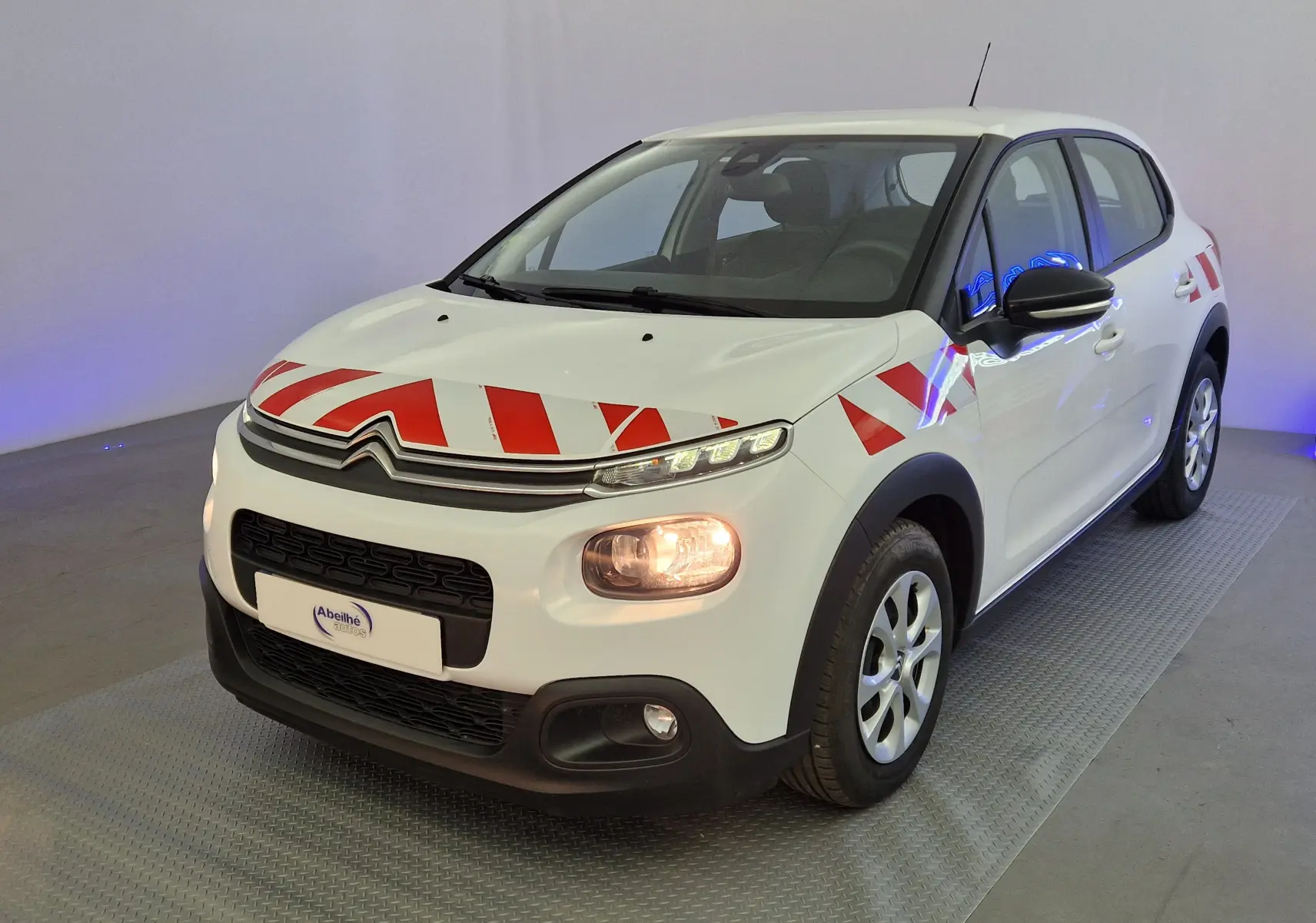Vue 3/4 avant droite d'une Citroën C3 Société blanche avec bandes rouges de signalisation sur capot et ailes.