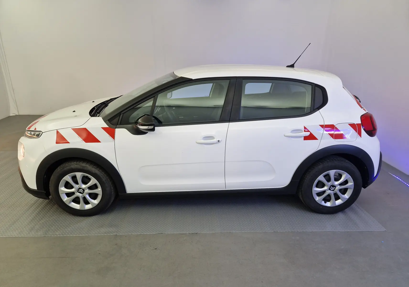 Vue de profil côté gauche d'une Citroën C3 blanche avec bandes rouges diagonales sur l'aile avant et arrière.