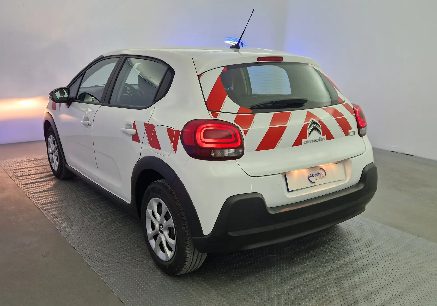 Vue 3/4 arrière droite d'une Citroën C3 Société blanche de 2019 avec bandes rouges diagonales sur la partie arrière.