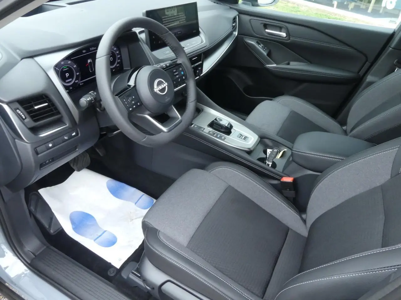 Intérieur du Nissan Qashqai 2025 vu côté conducteur, sellerie mixte gris et console centrale moderne avec volant multifonction.