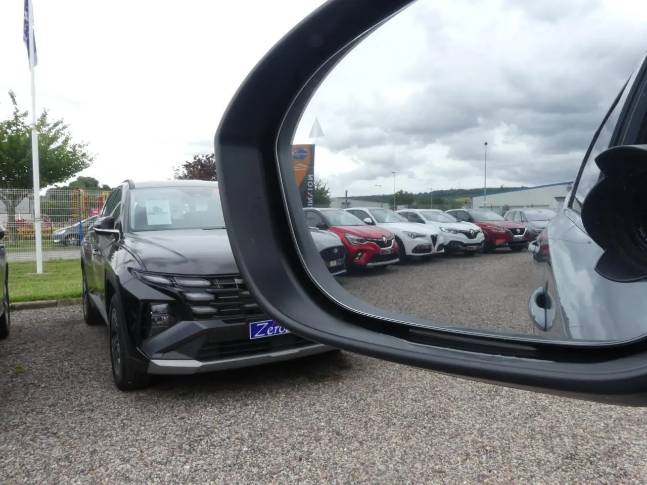 Vue en miroir du rétroviseur droit montrant un Nissan Qashqai gris métallisé de face sur un parking.