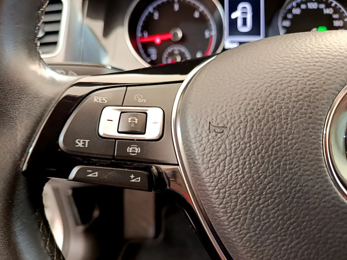 Gros plan sur la partie gauche du volant cuir de la Volkswagen Golf gris clair avec commandes de régulateur adaptatif.