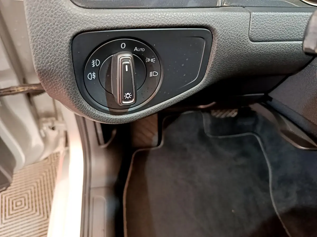 Gros plan sur le bouton de commande des phares noir dans l'habitacle côté gauche d'une Volkswagen Golf gris clair.