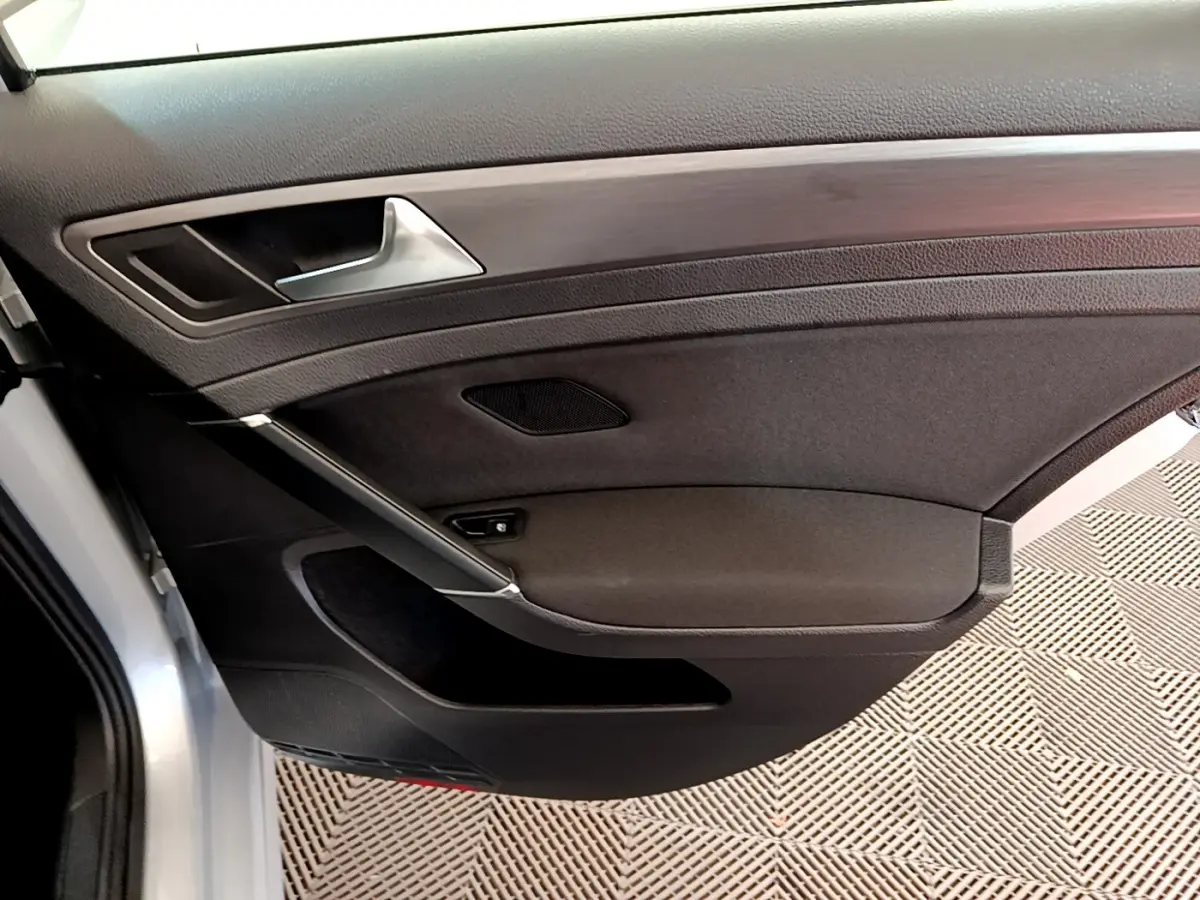 Gros plan sur la porte intérieure côté gauche de la Volkswagen Golf gris clair, avec poignée argentée et garniture noire.
