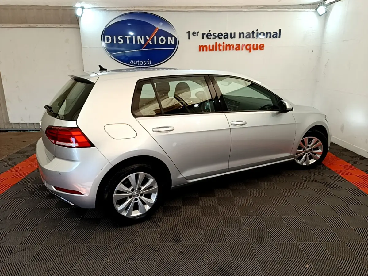 Volkswagen Golf gris clair vue de profil côté gauche dans un showroom avec logo Distinxion en arrière-plan.