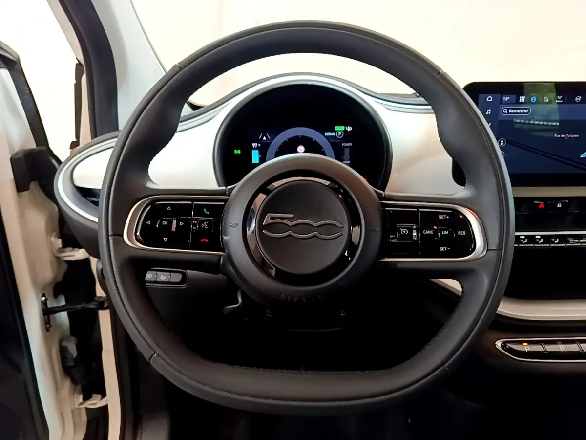 Vue intérieure centrée sur le volant noir de la Fiat 500 électrique blanche avec tableau de bord digital et écran tactile.