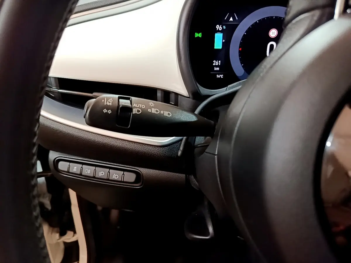 Gros plan sur le combiné d'instruments numérique et la commande des phares à gauche du volant dans le tableau de bord blanc de la Fiat 500 électrique blanche.