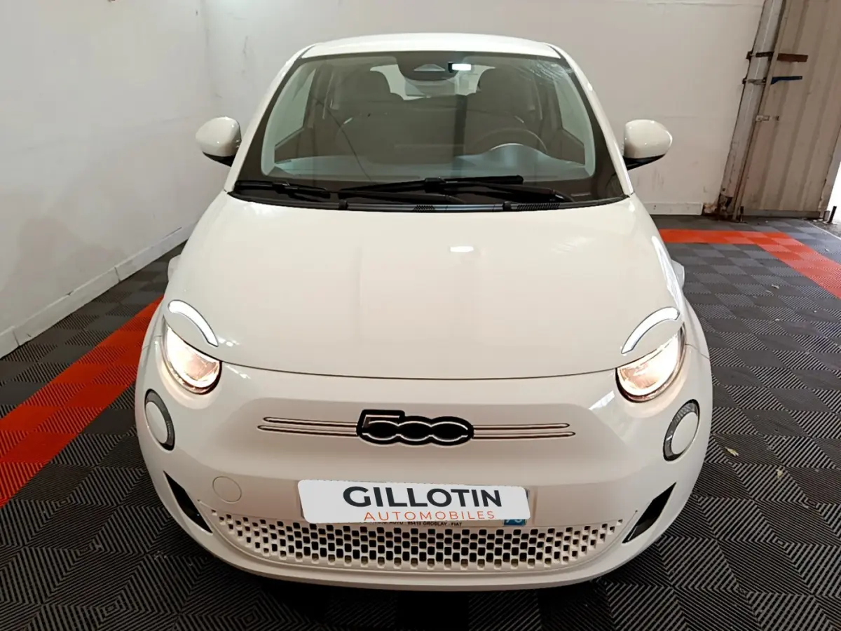 Vue avant d'une Fiat 500 électrique blanche Icône 42kWh avec phares allumés en intérieur.