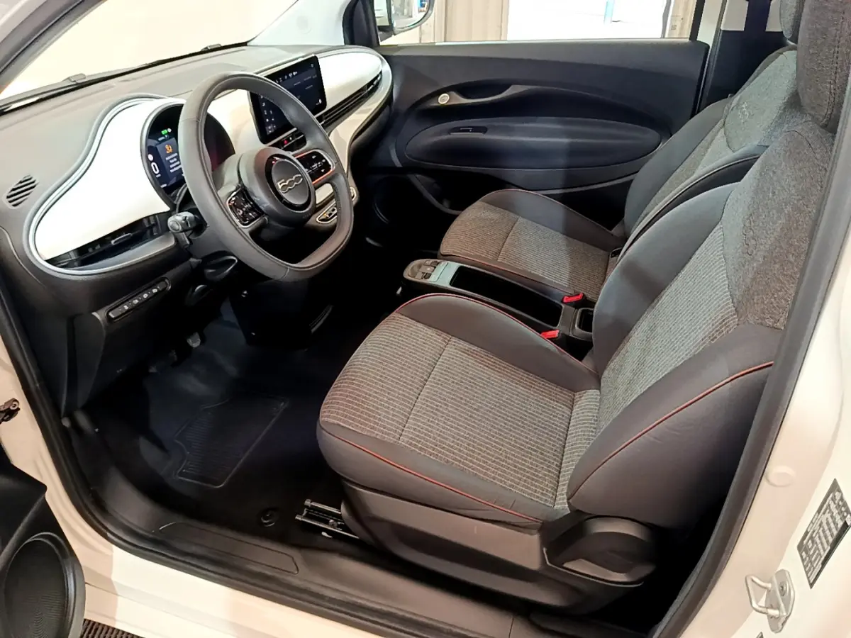 Intérieur avant droit de la Fiat 500 Icône 42kWh 2022 blanc, avec tableau de bord blanc et sièges gris à surpiqûres rouges.