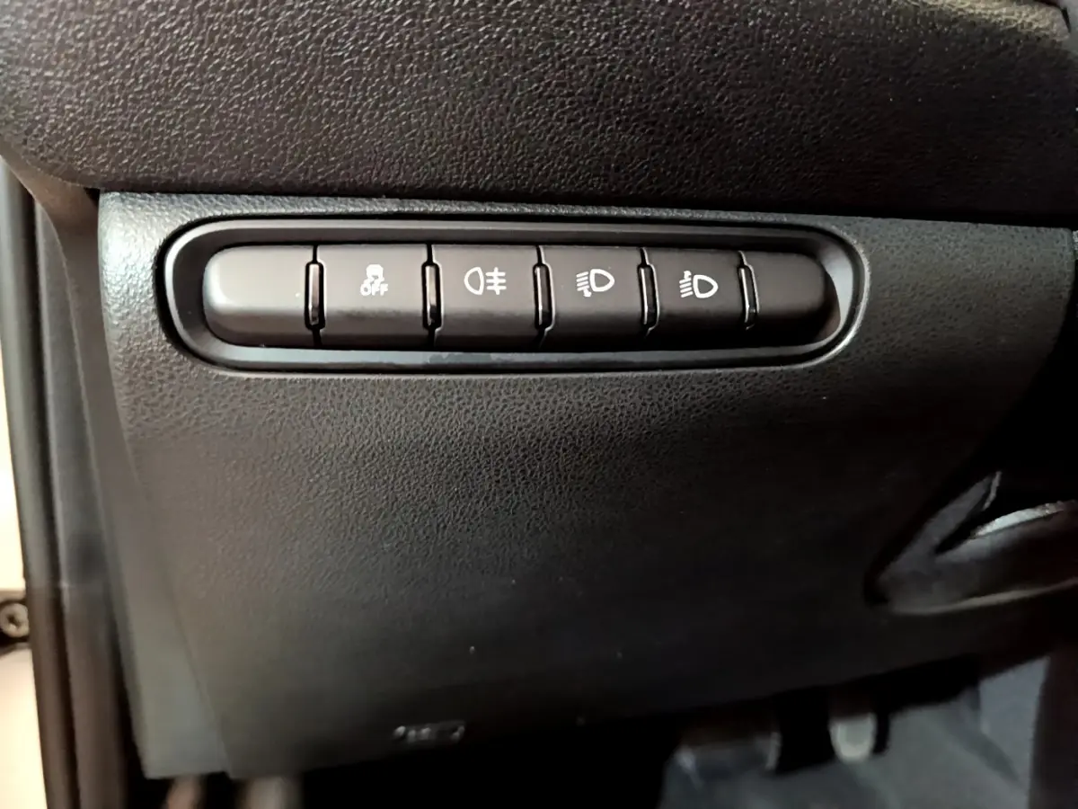 Gros plan sur les boutons de commande des phares et de l'antipatinage dans l'habitacle noir d'une Fiat 500 électrique blanche 2022.