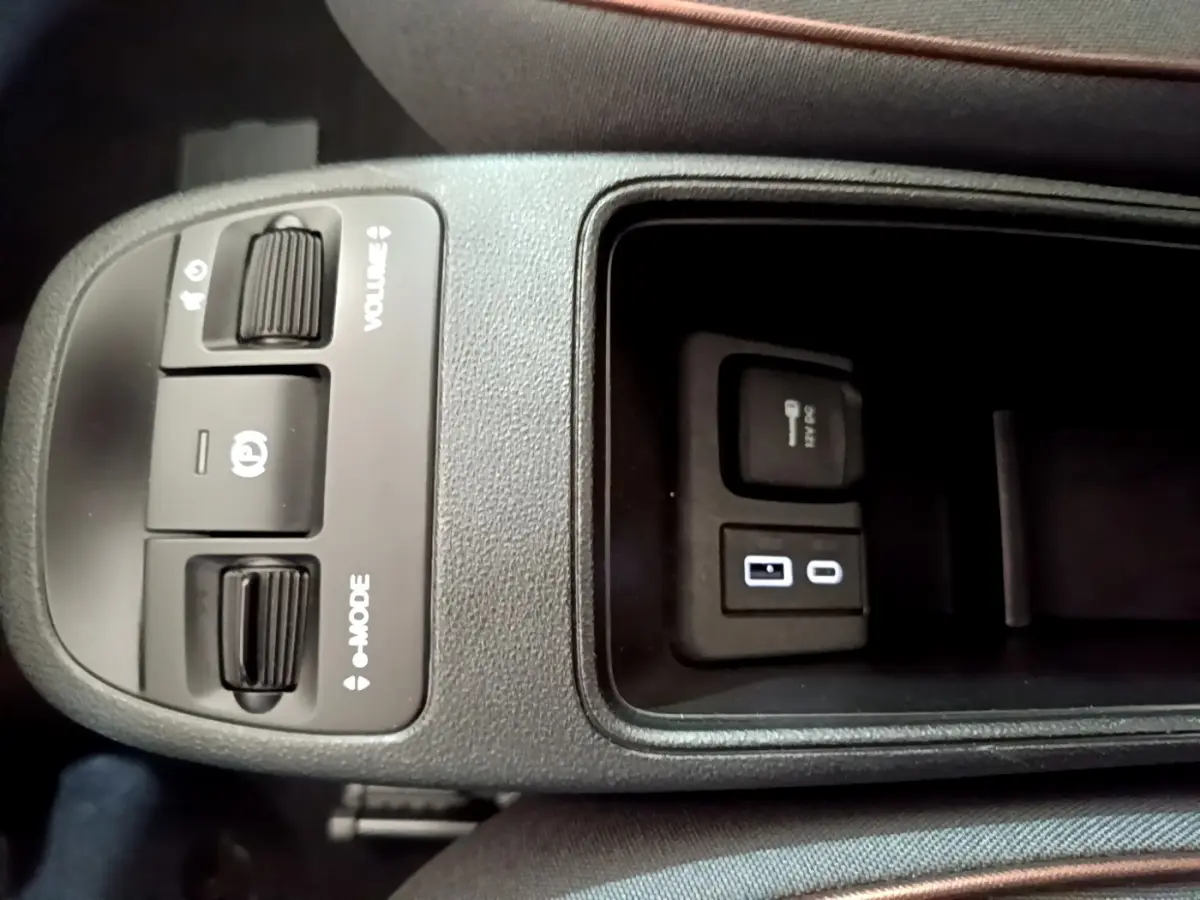 Vue rapprochée de la console centrale noire de la Fiat 500 électrique blanche, avec commandes volume, mode et prises USB et 12V.