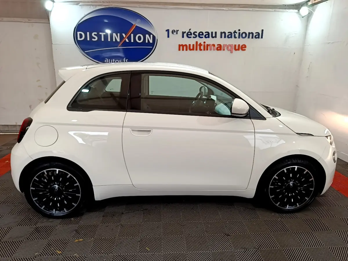 Profil côté droit d'une Fiat 500 électrique blanche 42kWh Icône avec jantes noires stylisées en intérieur showroom.