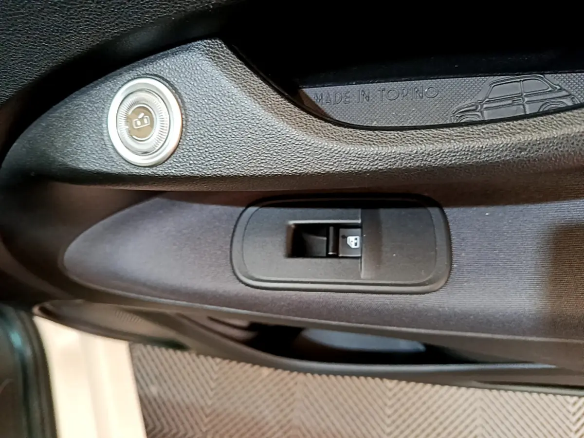 Gros plan sur la commande de lève-vitre côté gauche de la porte noire intérieure d'une Fiat 500 électrique blanche.