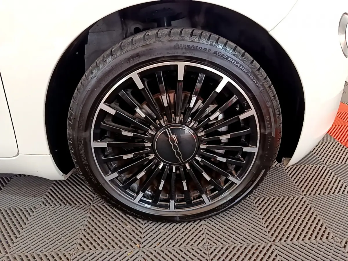 Gros plan sur la roue avant droite noire à jantes stylisées d'une FIAT 500 électrique blanche 2022.