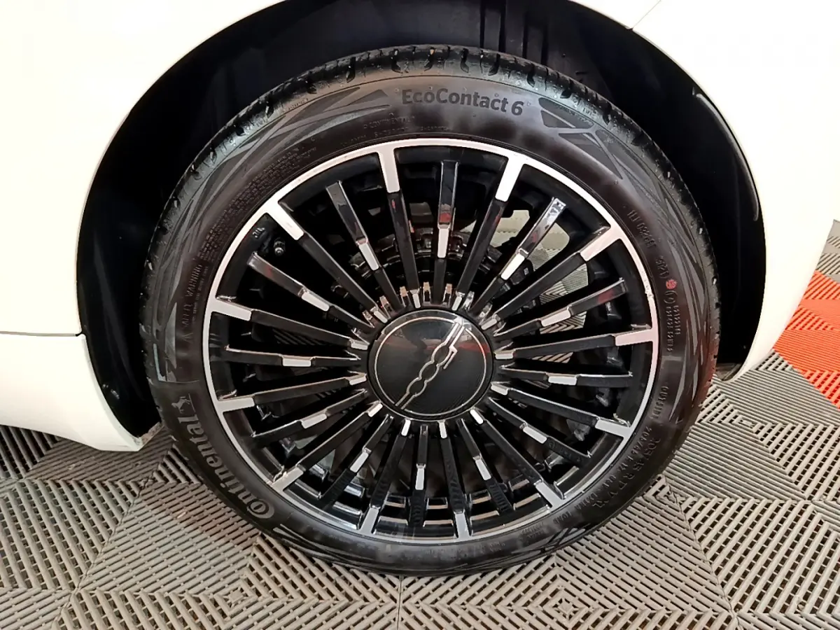 Gros plan sur la roue avant gauche de la FIAT 500 blanche électrique, jante noire à rayons fins avec logo central.