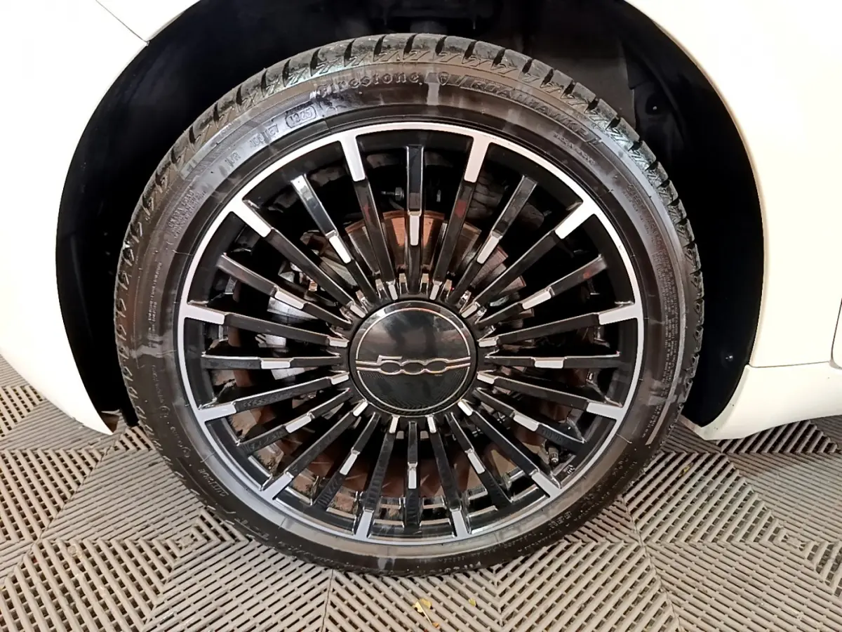 Gros plan sur la roue avant droite blanche d'une FIAT 500 électrique avec jante noire à rayons fins et logo central 500.
