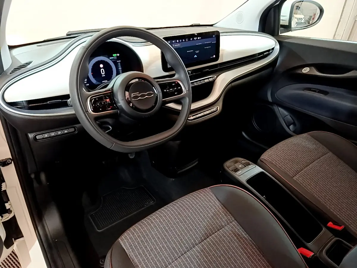 Vue intérieure côté conducteur de la Fiat 500 électrique blanche, tableau de bord moderne avec écran tactile central.