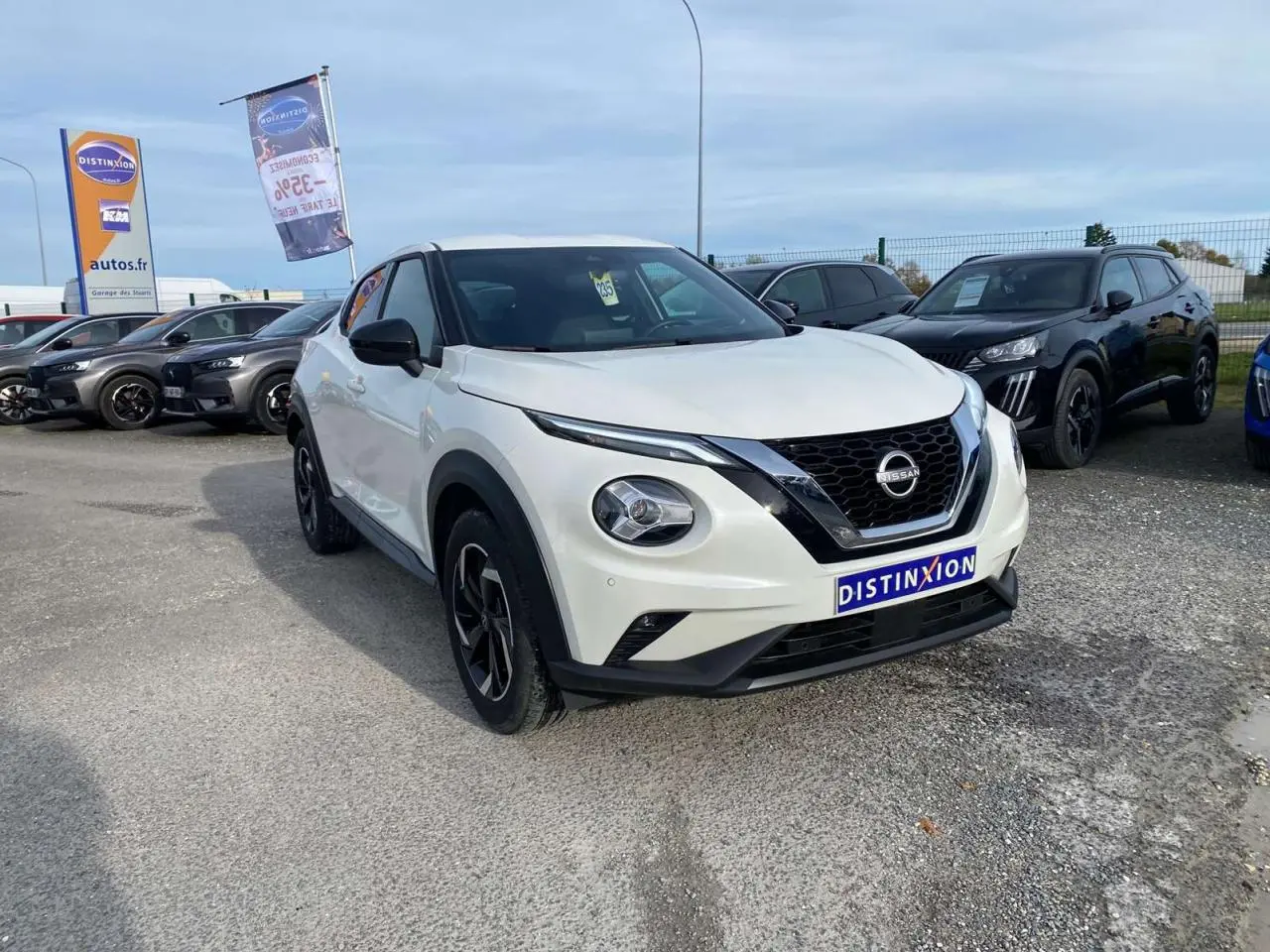 Nissan Juke blanc perle vu en 3/4 avant droit sur parking, avec calandre noire et jantes alliage noires.