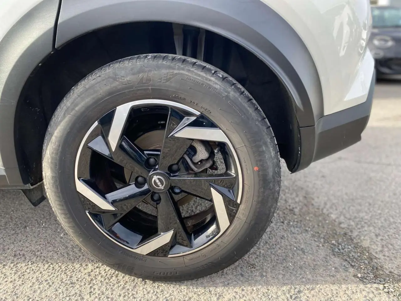 Gros plan sur la roue avant gauche du Nissan Juke blanc perle 2024 avec jante noire et argentée au design moderne.