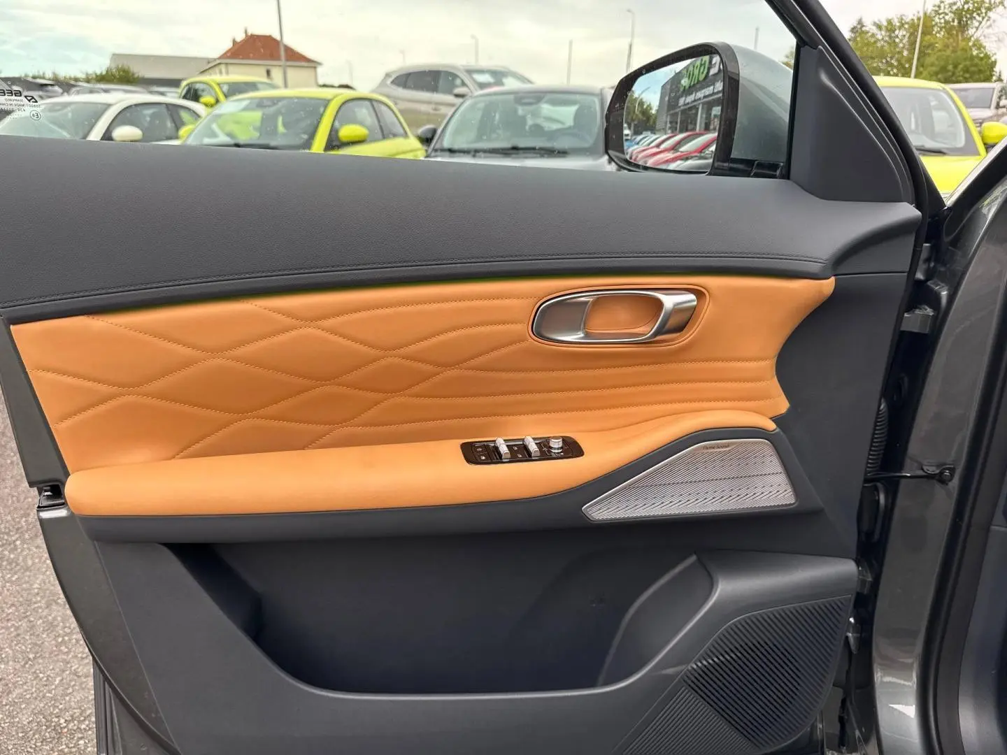 Vue intérieure côté gauche de la porte avant d’un Geely STARRAY 2026 Volcanic Grey avec garniture cuir marron et haut-parleur Harman Kardon.