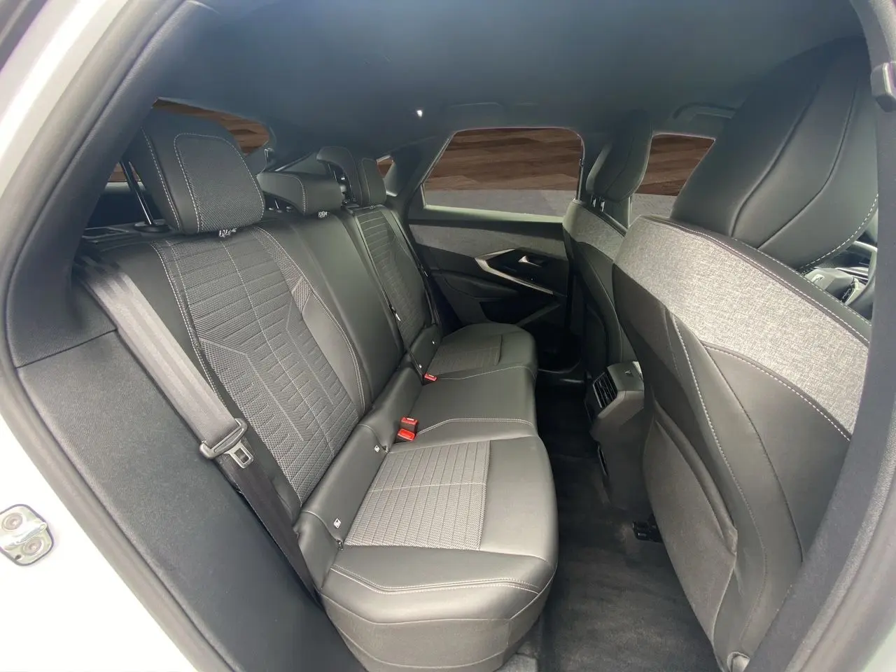Vue intérieure arrière du Peugeot 3008 2024 blanc Okenite, sièges noirs en cuir et tissu avec surpiqûres contrastées.