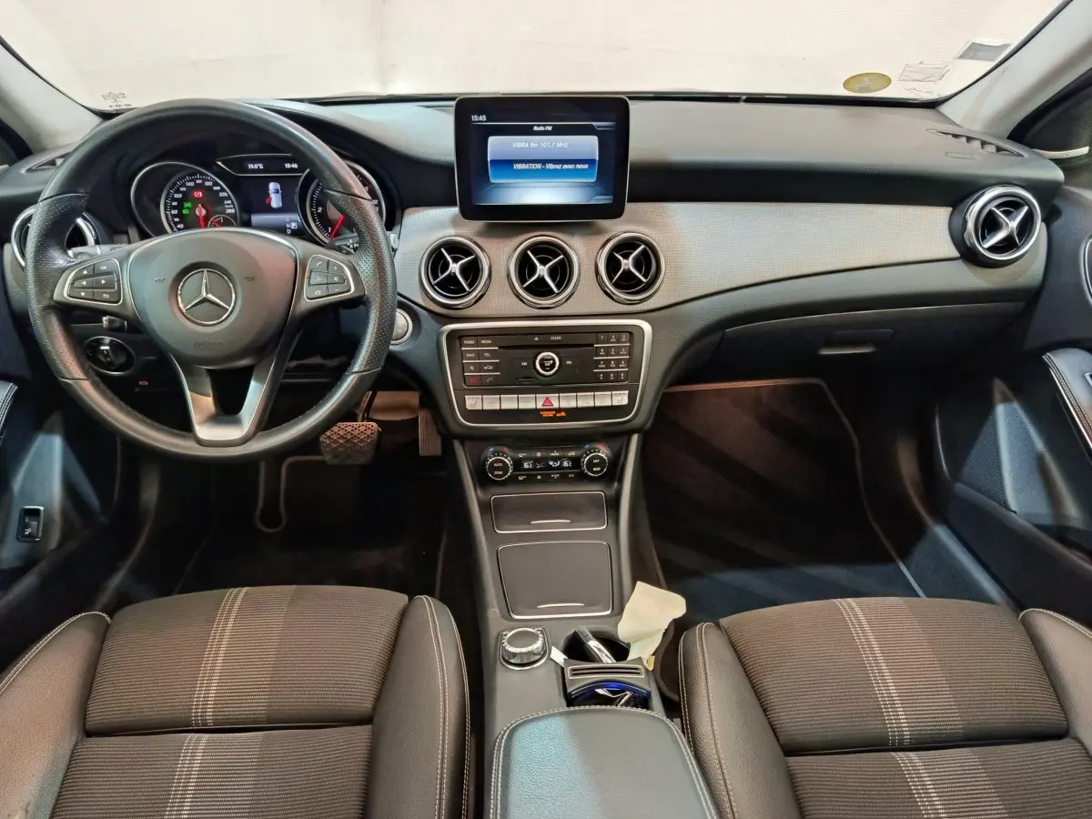 Vue intérieure frontale du tableau de bord et volant cuir noir d'une Mercedes GLA 220 d Business Exec 2018 avec écran central et aérateurs ronds.