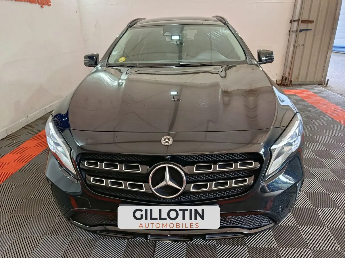Vue frontale d'un Mercedes GLA 220 d noir avec calandre distinctive et phares LED, stationné en intérieur.