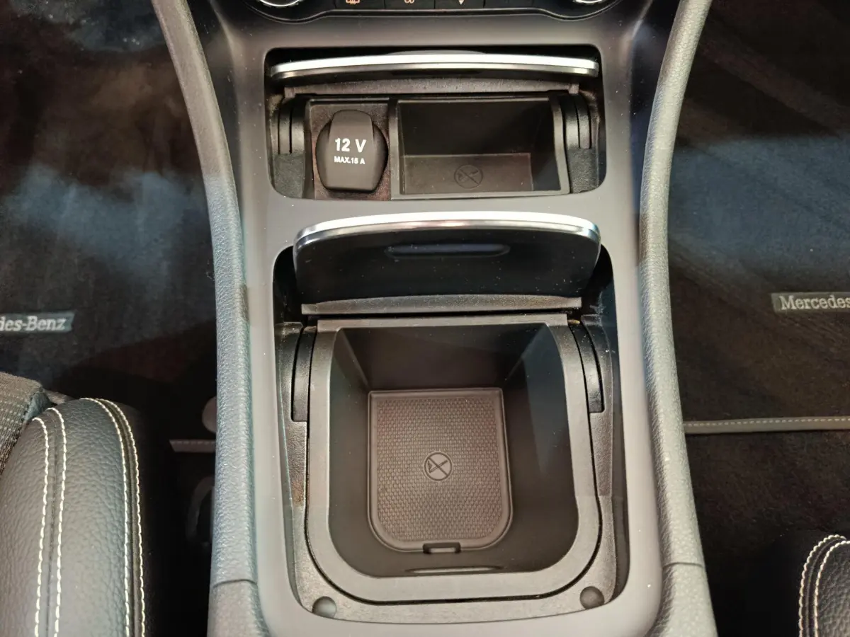 Vue plongeante sur la console centrale noire du Mercedes GLA 220 d, avec prise 12V et compartiment de rangement ouvert.