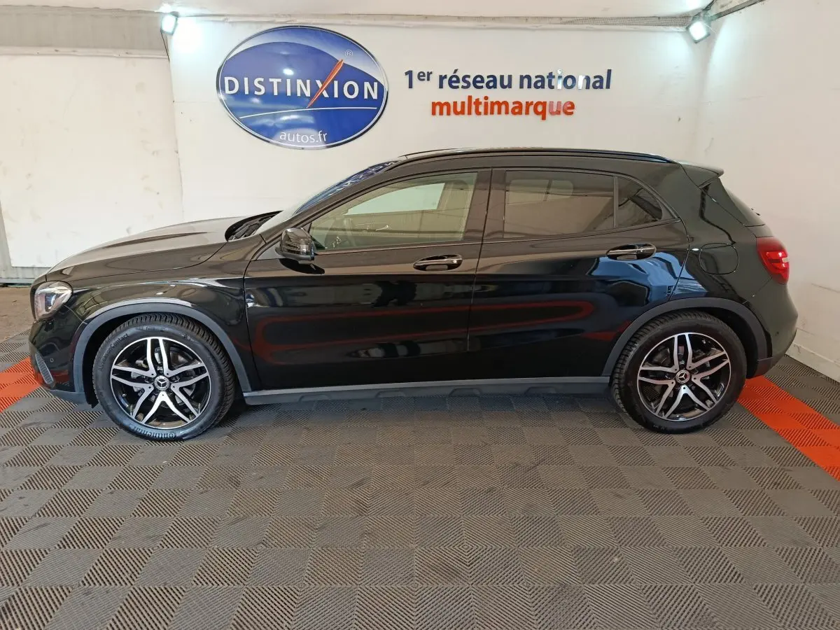 Vue de profil côté gauche d'un Mercedes GLA 220 d noir brillant avec jantes alliage et vitres teintées en intérieur showroom.