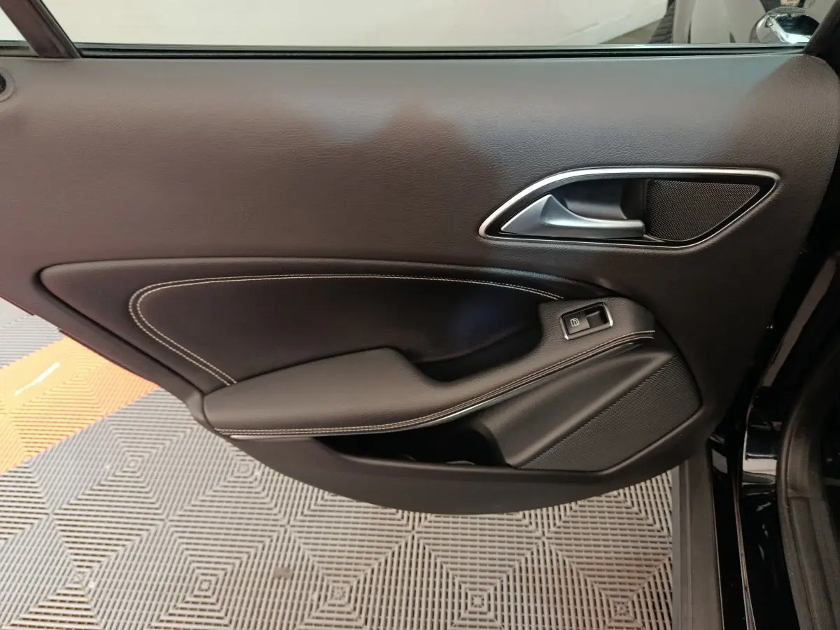Gros plan sur la porte côté gauche noire du Mercedes GLA 220 d Business Exec avec surpiqûres blanches et poignée argentée.
