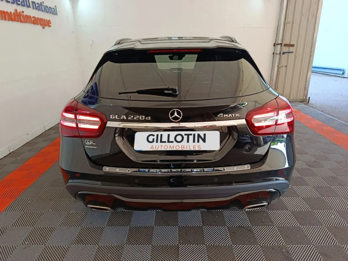 Vue arrière d'un Mercedes GLA 220 d noir avec feux LED allumés et logo 4Matic visible sur parking intérieur.
