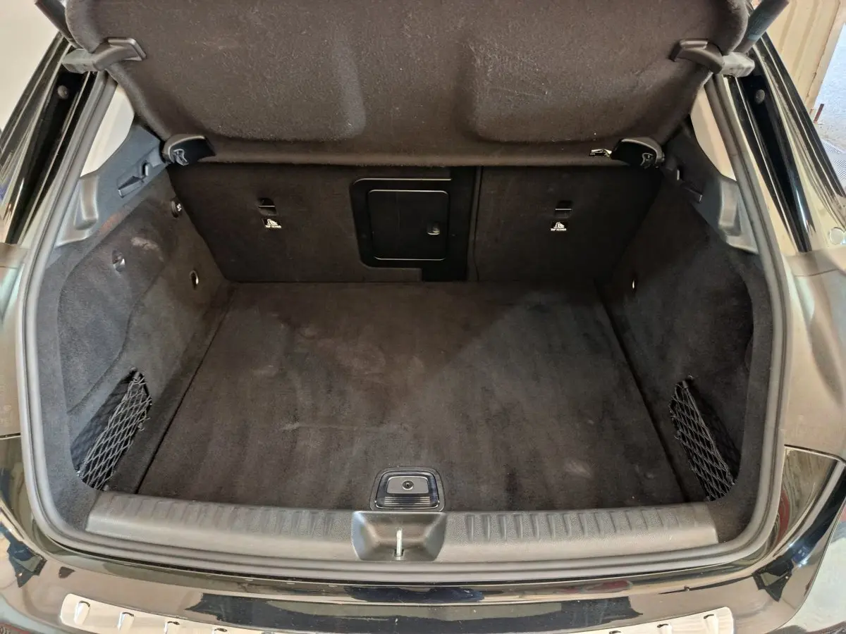 Coffre ouvert vu de l'arrière d'un Mercedes GLA 220 d noir, intérieur propre avec filet de rangement sur les côtés.