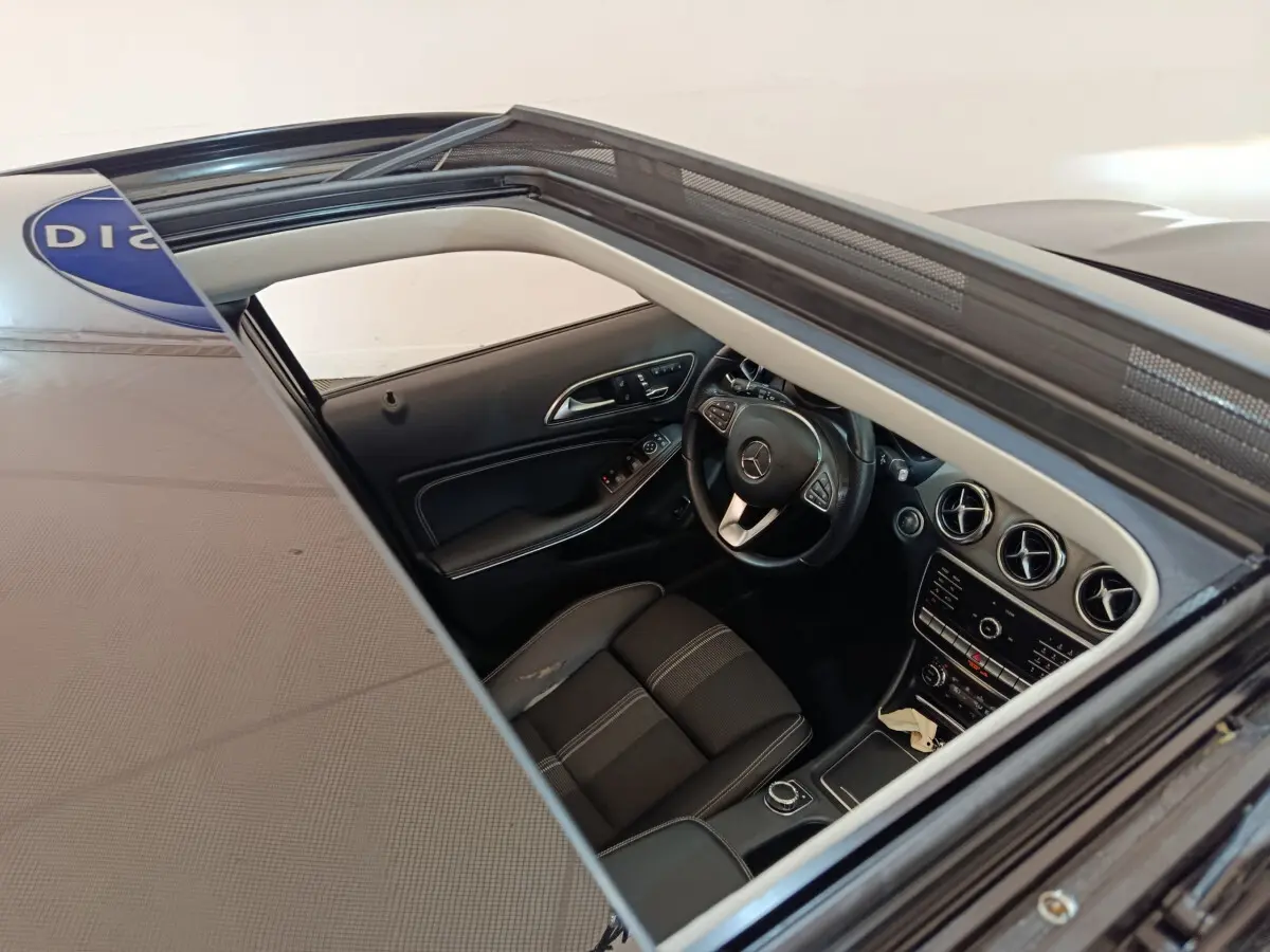 Vue intérieure par le toit ouvrant d'un Mercedes GLA noir, montrant le volant cuir multifonctions et le tableau de bord moderne.