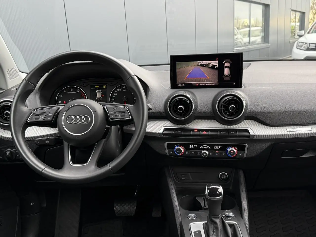 Intérieur Audi Q2 35 TFSI 2023 vu du conducteur, volant cuir, écran central affichant la caméra de recul.