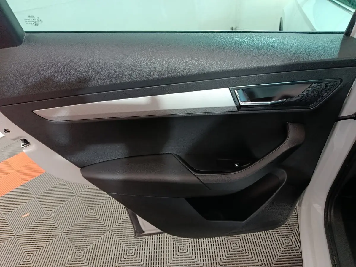 Vue côté gauche de la porte intérieure noire et grise du Skoda Karoq 2024 avec poignée et commande de fenêtre électrique.